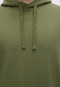 Sweat à capuche vert olive avec cordons tressés épais et logo « HUGO » embossé centré sous l'encolure.