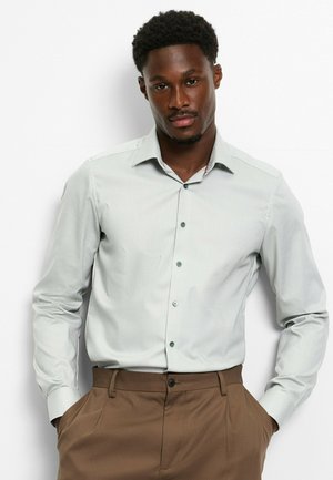 Hellgraues Langarmhemd mit Button-Down-Kragen und subtiler Textur, kombiniert mit braunen Hosen. Mit passenden Knöpfen.