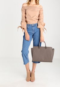 Béžový top bez ramínek s volnými rukávy, modré vysoké zkrácené džíny, béžové boty na podpatku s otevřenou špičkou a šedá kabelka s pevným uchy.