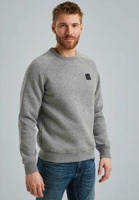 Grauer Rundhalsausschnitt-Pullover aus weichem Stoff, mit gerippten Bündchen und Saum sowie einem kleinen schwarzen Logopatch auf der Brust.