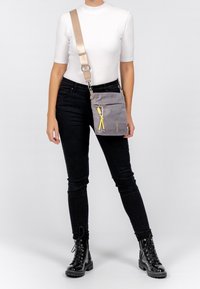 Šedá crossbody taška vyrobená z textilu s texturovaným povrchem, s žlutým táhnutím zipu a odepínacím popruhem.