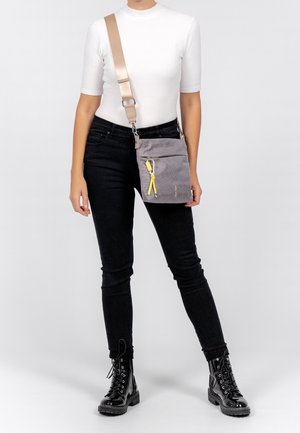 Šedá crossbody taška vyrobená z textilu s texturovaným povrchem, s žlutým táhnutím zipu a odepínacím popruhem.