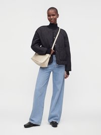 Personne portant une veste matelassée noire, un jean large bleu clair, des chaussures noires, et portant un sac à bandoulière beige.