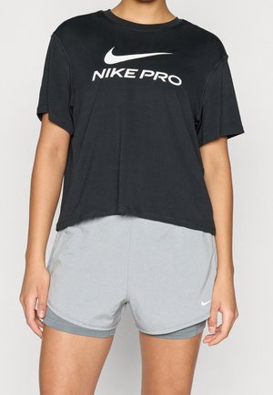 Personne portant un t-shirt Nike Pro noir et un short de sport Nike gris clair sur un fond uni.