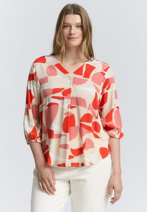 Blouse multicolore avec un décolleté en V, des manches trois-quarts et des motifs abstraits rouges, roses et crème sur un tissu léger.