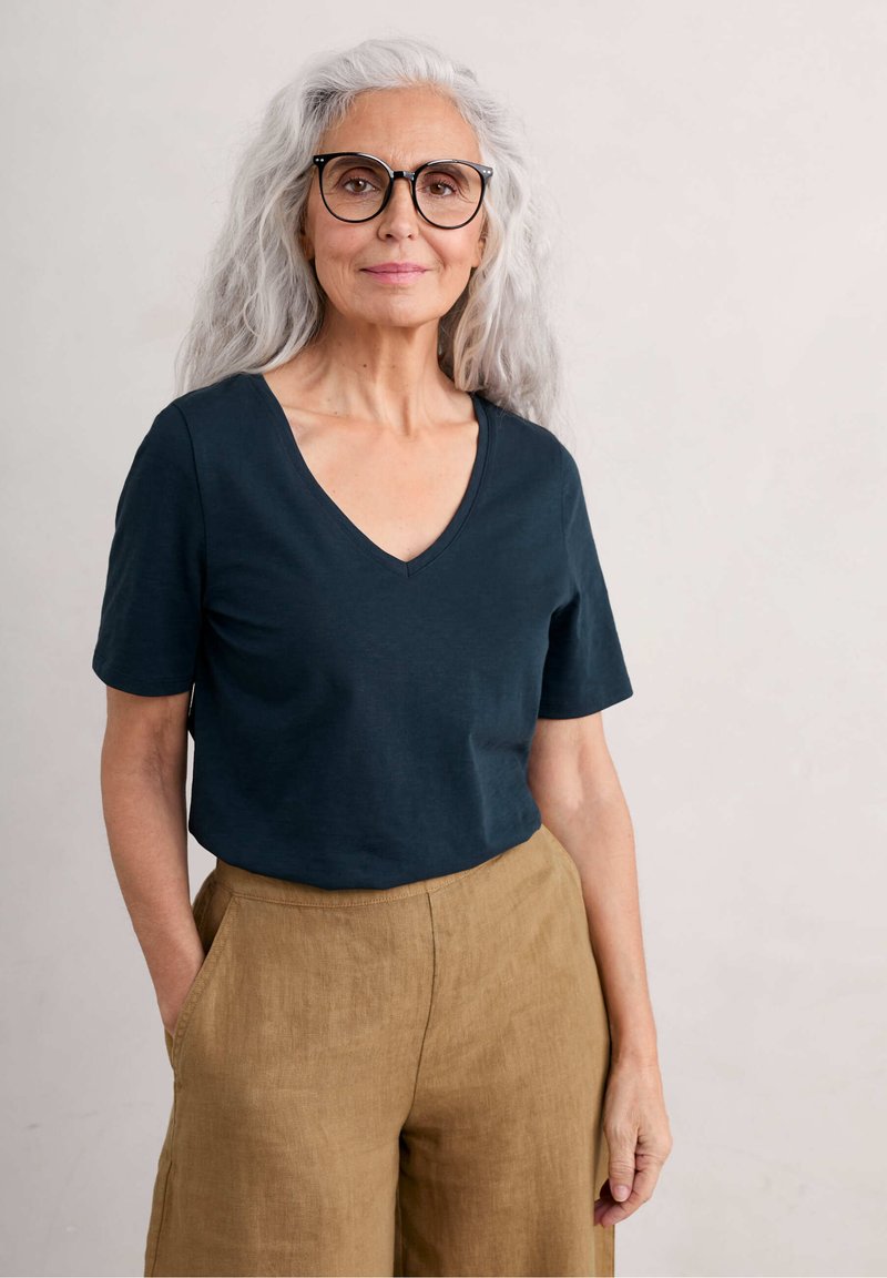 Dark green V-neck t-shirt paired with light brown, wide-leg linen trousers. The loose fit emphasizes comfort and breathability.