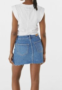 Džínová sukně s třepeným lemem, dvěma zadními kapsami a dobře padnoucím pasem, spojená s bílým tílkem bez rukávů.