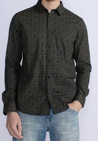 Camicia con maniche lunghe e bottoni in tessuto blu scuro con motivo dorato. Presenta un colletto, una tasca sul petto e bottoni lungo la parte anteriore.