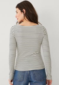 Langärmliges, geripptes Shirt in Creme mit marineblauen Streifen, mit Rundhalsausschnitt und taillierter Passform, kombiniert mit Jeans.