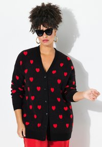 Schwarze Strickjacke mit roten Herzmustern, mit V-Ausschnitt, langen Ärmeln und Knöpfen an der Front; weicher Stoff und lockere Passform.