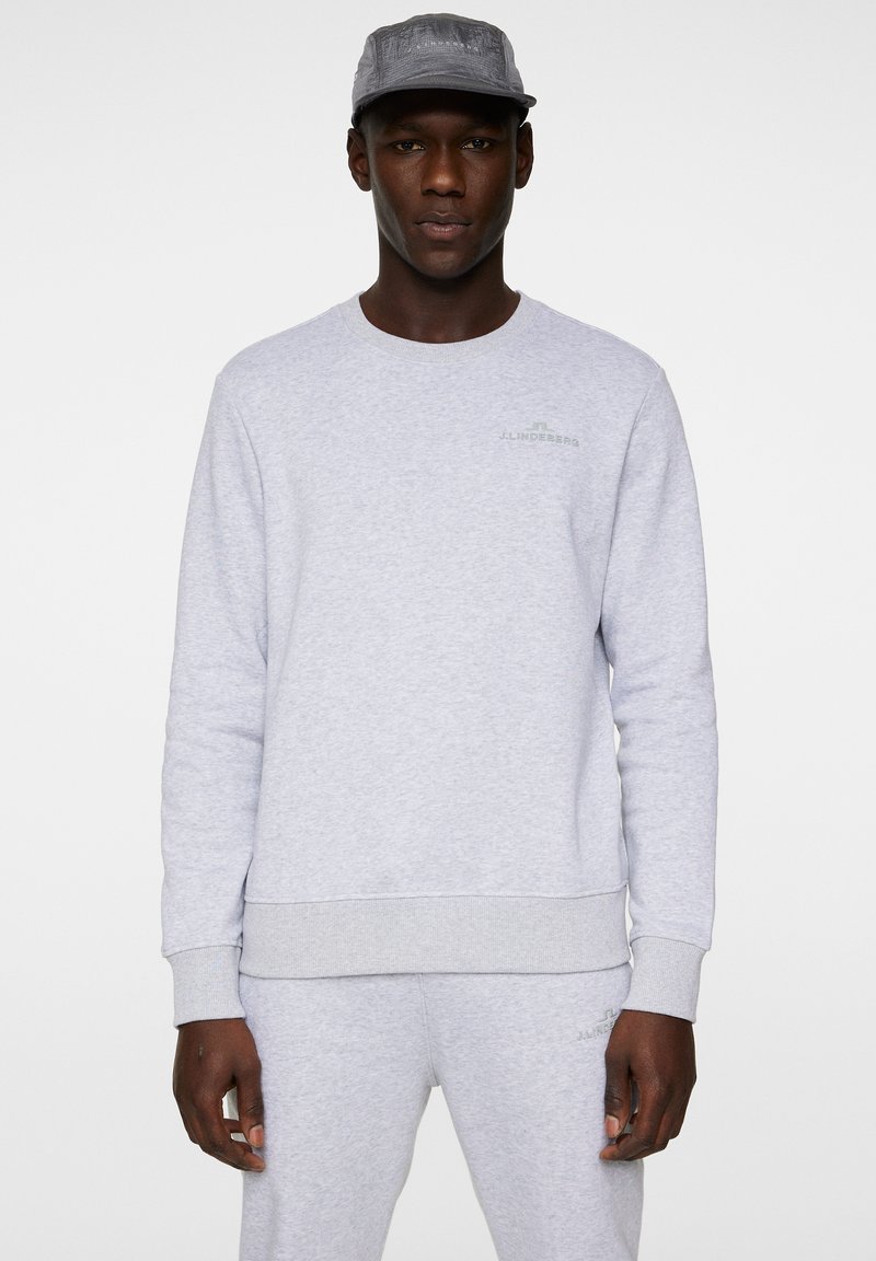 Ljust grå sweatshirt i bomullsblandning med ribbad mudd och nederkant. Litet grönt logotyp på bröstet, slät textur, minimalistisk design.