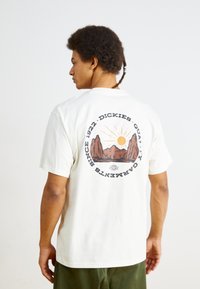 White cotton T-shirt featuring a round graphic on the back with mountains, sun, and text. Short sleeves, relaxed fit, and crew neck design.