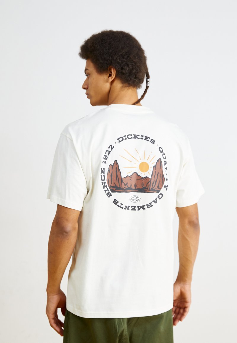 White cotton T-shirt featuring a round graphic on the back with mountains, sun, and text. Short sleeves, relaxed fit, and crew neck design.
