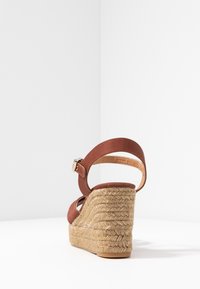 Hnědé espadrilové sandály na klínu s texturovanou juty podrážkou, nastavitelním popruhem a otevřenou zadní částí, která vytváří elegantní vzhled hladkého textilního svrchního materiálu.