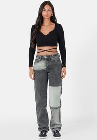 Top corto de manga larga negro con canalé, combinado con vaqueros relajados de patchwork en gris que presentan un parche en la rodilla de color gris claro y detalles clásicos de denim.