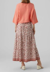 Top corto de color coral con mangas anchas, combinado con una falda larga y estampada con motivos florales y un borde colorido en el dobladillo.