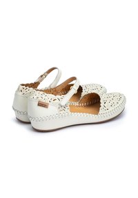 Weiße Lederschuhe mit kunstvollen Ausschnitten, verstellbarem Riemen und genähten Verzierungen entlang der Sohle. Abgerundete Zehenpartie und flache Sohle.