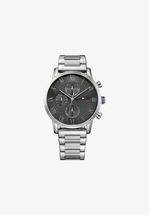 Zilverkleurig metalen polshorloge met zwarte wijzerplaat, drie subdials voor dag, 24 uur en datum, Romeinse cijfers en Tommy Hilfiger-logo op 3 uur.