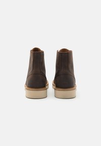 Botines de cuero marrón con un acabado liso, suela de goma beige en contraste y un sencillo detalle de costura en la parte trasera.