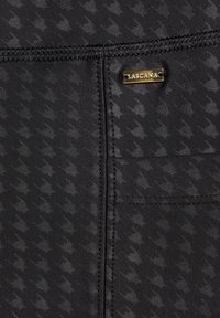 Black activewear fabric featuring a subtle houndstooth pattern. Includes a gold logo tag and smooth texture with visible stitching details.