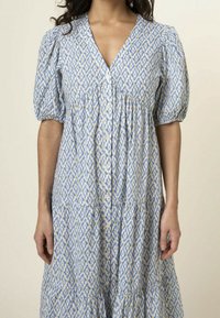 Blue and white patterned dress with short puff sleeves, V-neckline, button-down front, and gathered waist detail. Features a tiered skirt.