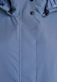 Mėlynas paminkštintas švarkas su lygiu paviršiumi, turintis juodus snapus ir užtrauktuku uždaromą kišenę kairėje pusėje.