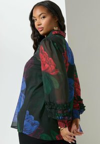 Blusa nera trasparente con motivo floreale, caratterizzata da rose rosse e blu, con polsini a ruffles e un colletto strutturato. Texture liscia in tutto il capo.
