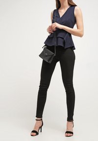 Námořnický peplum top, černé úzké kalhoty a černé sandály na podpatku se šněrováním. Top má design s překrytím, což vytváří vrstvený efekt a hladkou texturu.