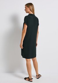 Zielona sukienka z krótkim rękawem, z kołnierzykiem, luźny krój, długość midi i miękka tekstura. Połączona z czarnymi sandałami z paskami na kostce.