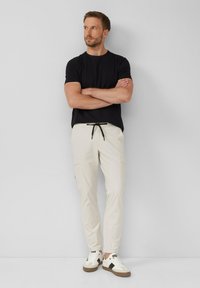 Lichtbeige cargobroek met tailling, slim fit en zijzakken, gecombineerd met een zwarte t-shirt met korte mouwen en witte sneakers.