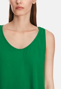 Green cotton tank top with a scoop neckline and wide shoulder straps, featuring a smooth texture and tailored fit.