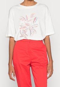 Camiseta blanca de corte suelto con un patrón de hojas en rosa y azul. Combinada con pantalones rojos brillantes, creando un contraste de color audaz.