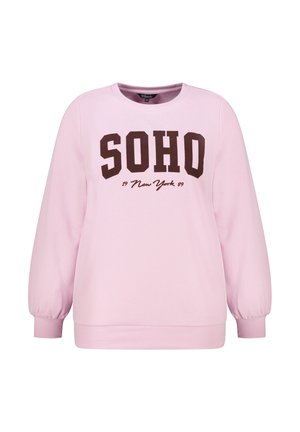 Sweatshirt rose clair à manches longues, avec des poignets côtelés, et « SOHO New York 1989 » imprimé en grandes lettres foncées sur le devant.