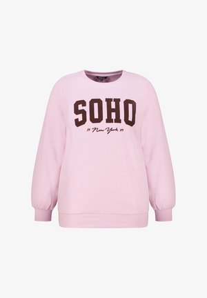 Sweatshirt rose clair à manches longues, avec des poignets côtelés, et « SOHO New York 1989 » imprimé en grandes lettres foncées sur le devant.