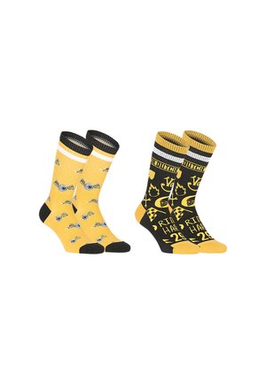 Deux paires de chaussettes montantes jaunes et noires, l'une avec des motifs d'appareils photo et des orteils noirs, l'autre avec des motifs graphiques et des textes variés.