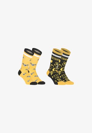 Deux paires de chaussettes montantes jaunes et noires, l'une avec des motifs d'appareils photo et des orteils noirs, l'autre avec des motifs graphiques et des textes variés.