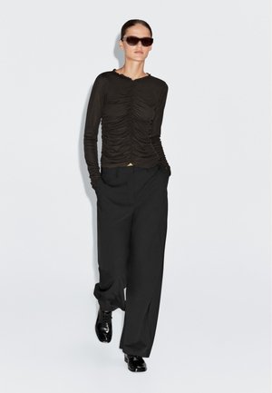 Long-sleeve dark brown top with gathered texture, round neckline, paired with black wide-legged trousers and sleek black shoes.