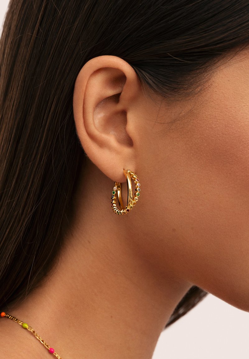 Los pendientes de aro en tono dorado presentan un diseño retorcido con pequeñas piedras preciosas de colores a lo largo del borde exterior. Acabado texturizado y brillante.