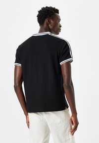 Svart pikétröja med vit krage och randiga detaljer, tillverkad av textil med struktur, med avslappnad passform och korta ärmar.