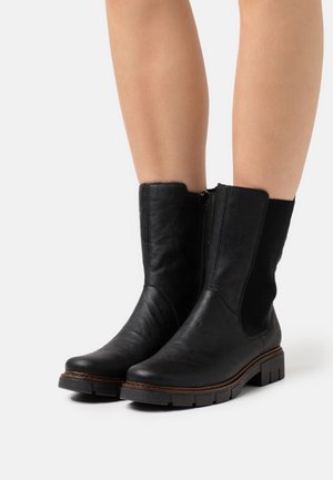 Botines negros de cuero liso con cremallera lateral, paneles elásticos y suela de goma texturizada para mejor agarre, con costuras en contraste.