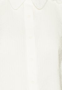 White button-up shirt featuring a textured fabric, pointed collar, and subtle vertical stripes. Includes buttons down the front.