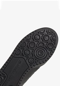 Svart gummiskosula med cirkulära och hexagonala mönster, med präglade logotyp-accenter och texturerade sektioner för grepp.