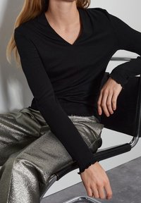 Svart ribbad långärmad topp med djup V-ringning och volangärmar, tillsammans med glänsande, silvermetalliska vida byxor.