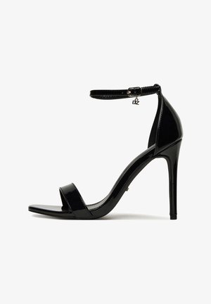 Sandalo con tacco in vernice nera con cinturino sottile alla caviglia, punta aperta e finitura lucida. Presenta un ciondolo metallico sul cinturino.