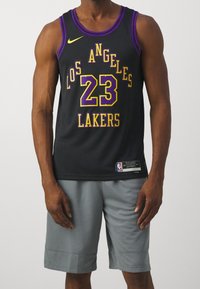 Canotta da basket nera con accenti viola e oro; presenta la scritta "LOS ANGELES LAKERS" e il numero "23." Indossata con pantaloni corti grigi. Logo Nike presente.