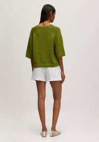 Groene gebreide pullover met korte mouwen, ribbelzoom en een ontspannen pasvorm. Gepaarde met witte shorts van een gestructureerde stof.