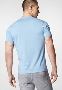 Jasnoniebieska bawełniana koszulka z krótkim rękawem, dopasowany krój i okrągły dekolt. Posiada małą metkę z tyłu. Noszona z szarymi dżinsami.