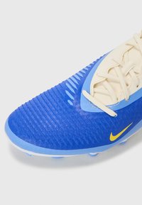 Blå fodboldstøvle med tekstureret overdel og syntetisk materiale. Har cremede snørebånd og et fremtrædende gult Nike-logo.