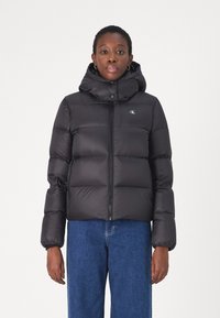 Black puffer jacket with a hood, zip-front closure, and elasticated cuffs. Features a logo on the chest and quilted design for insulation.