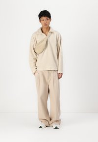 Fleece pullover i cremefarvet, med krave og lange ærmer, parret med beige bukser. En beige crossbody-taske hviler på den ene skulder.